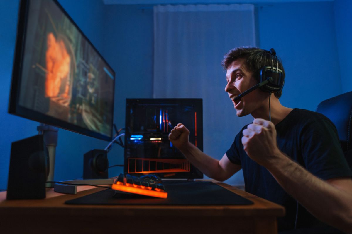 Gamer utilizando headset e computador de alto desempenho, reagindo intensamente durante partida online, ilustrando a importância da baixa latência para jogos competitivos.